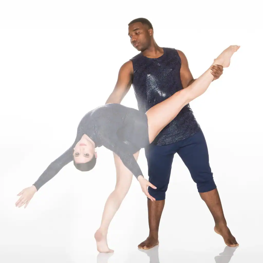 Two dancers perform a dramatic partnered lift on white background.