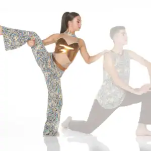 Dancer performing high leg stretch beside kneeling partner