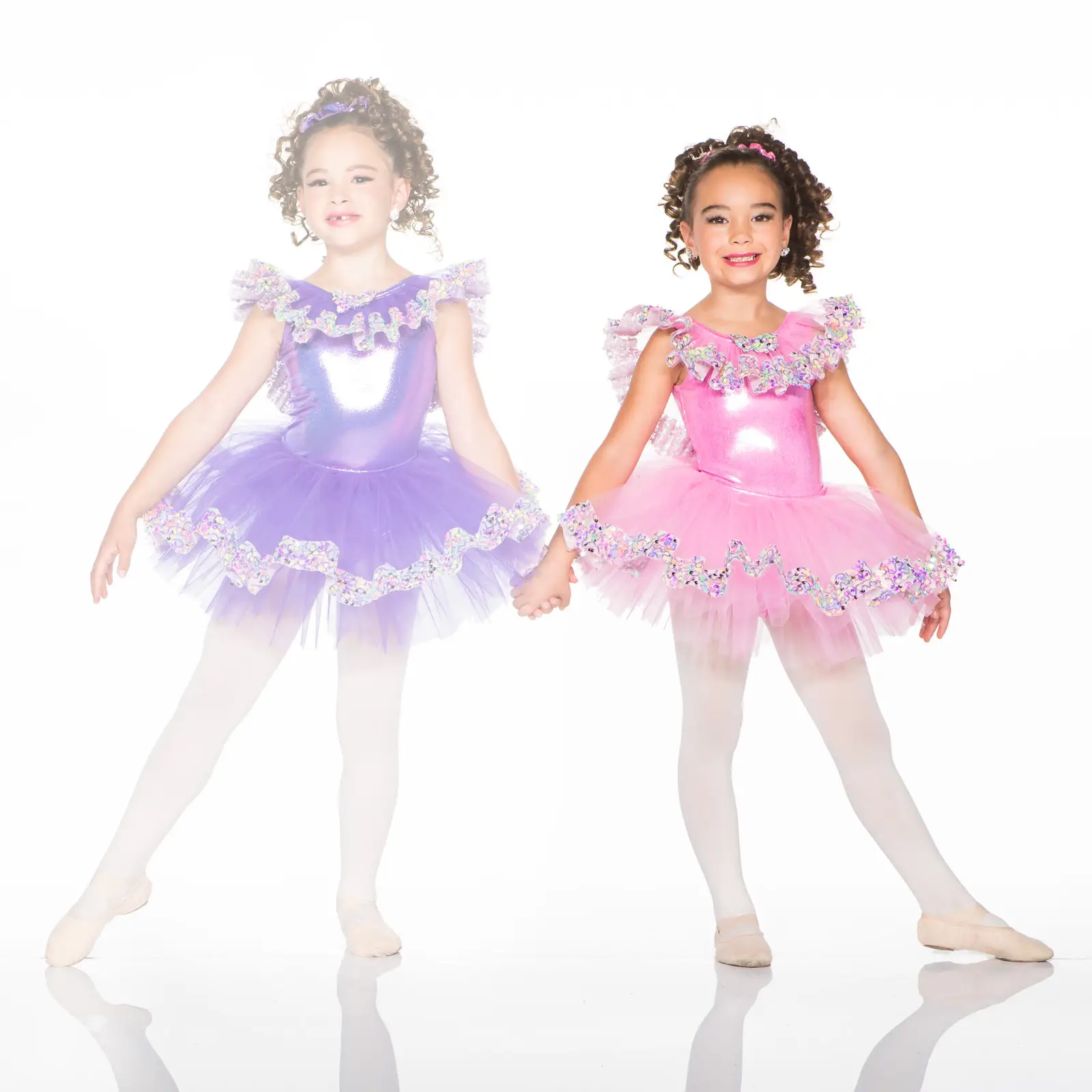 Two young ballerinas in pink and purple tutus holding hands