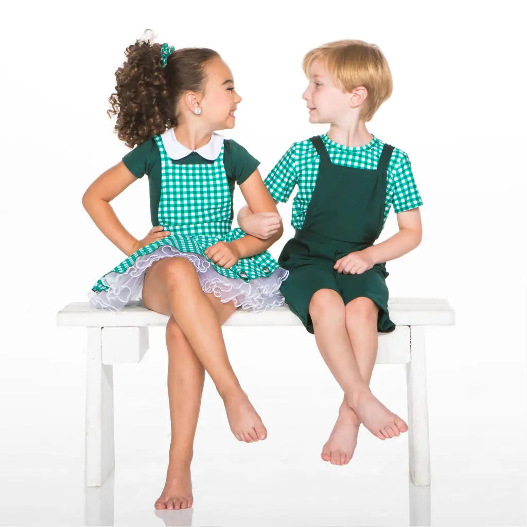 Two children in green checkered outfits sitting on a bench