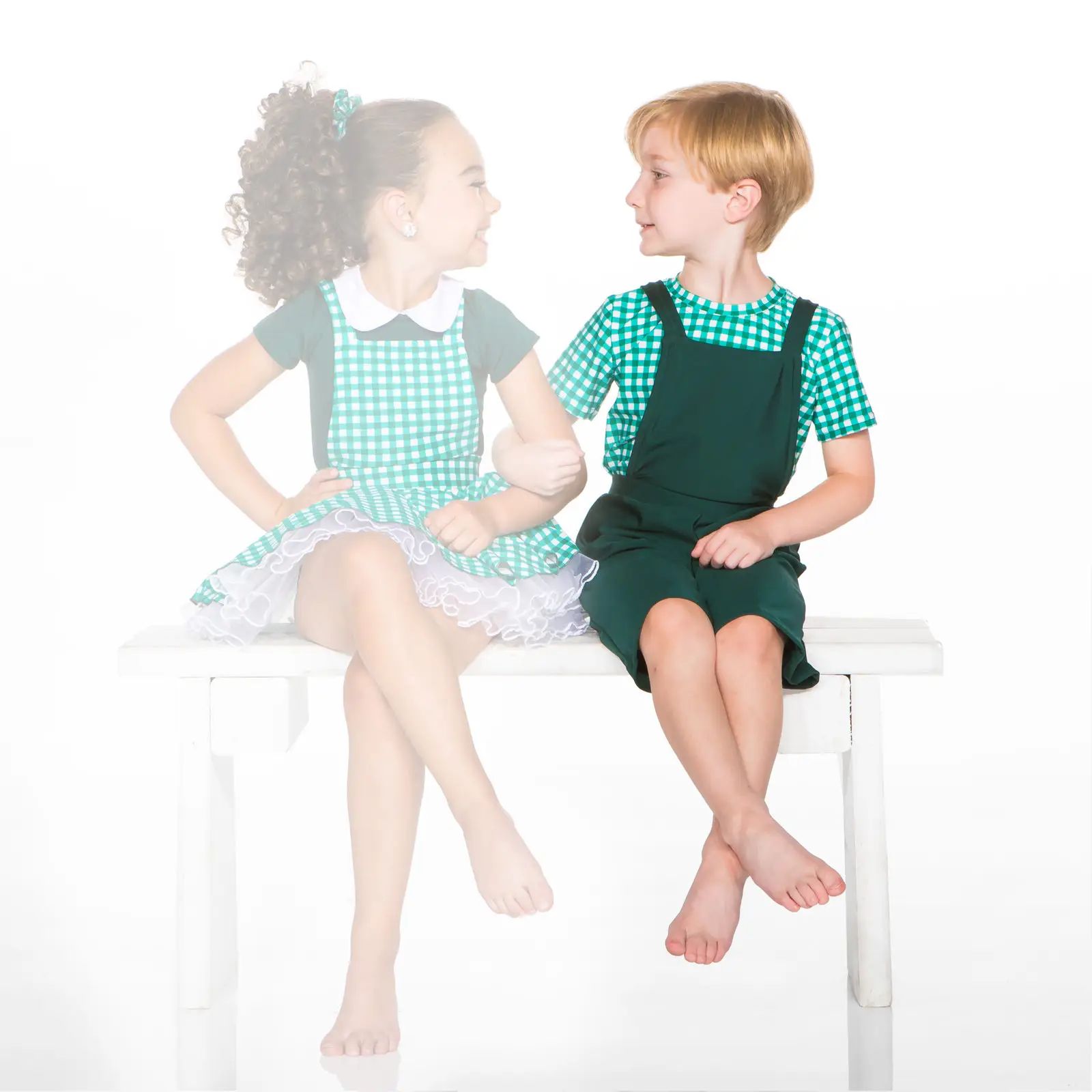 Two children in matching green outfits sit on a bench.