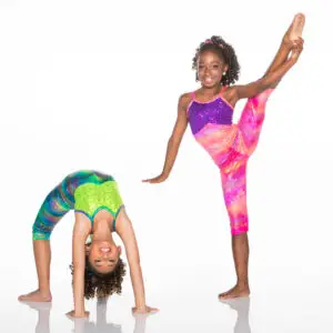 Two young gymnasts performing flexibility poses in colorful leotards