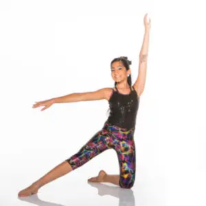 Young dancer kneeling in colorful leggings with arms extended